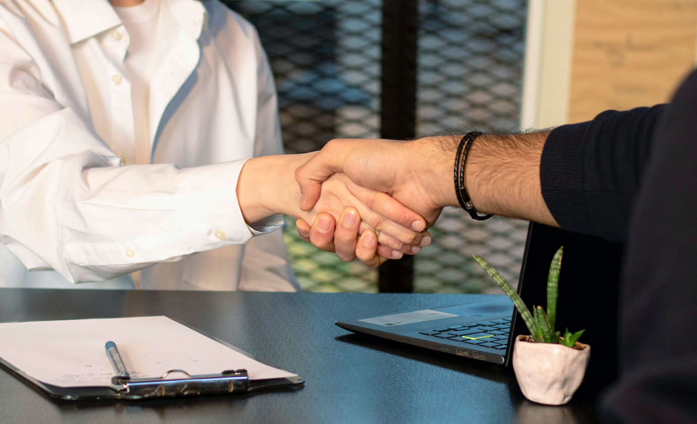 A man and woman shaking hands at a desk in an office during a management recruitment.